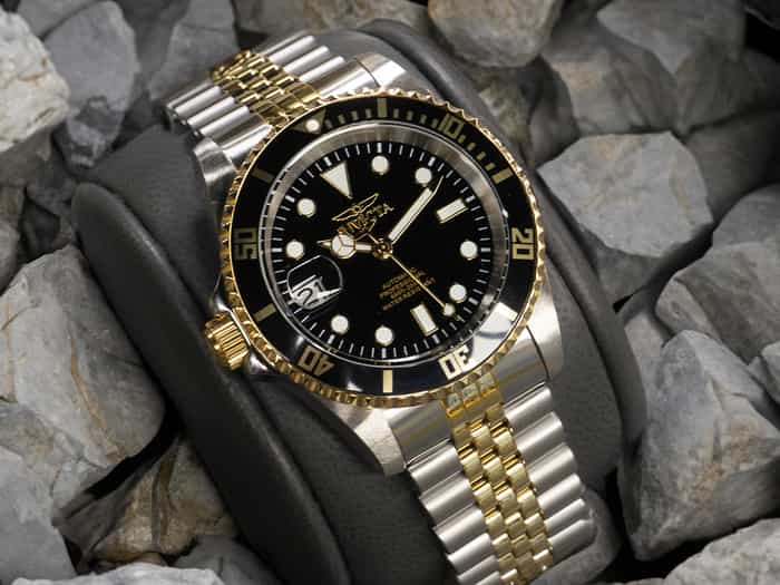 Image of a silver wristwatch with golden details, with a black clock face and white hour markers.