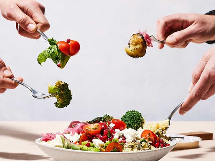 4 people with a fork digging into a salad bowl