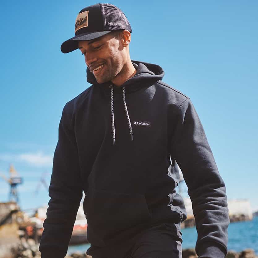 Columbia Man smiling outdoors in a hoodie and cap by the waterfront.