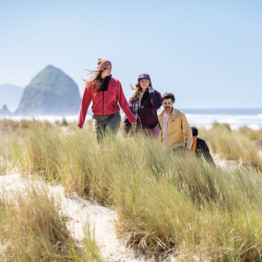 Columbia Group of people hiking through grassy dunes near the beach on a sunny day.