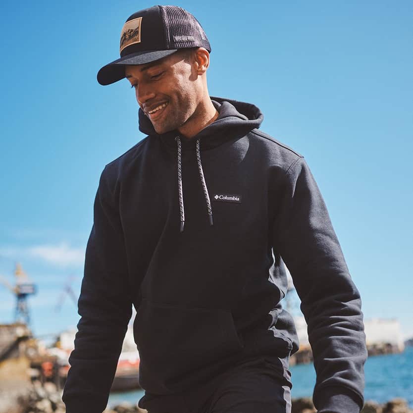Columbia Man smiling outdoors in a hoodie and cap by the waterfront.