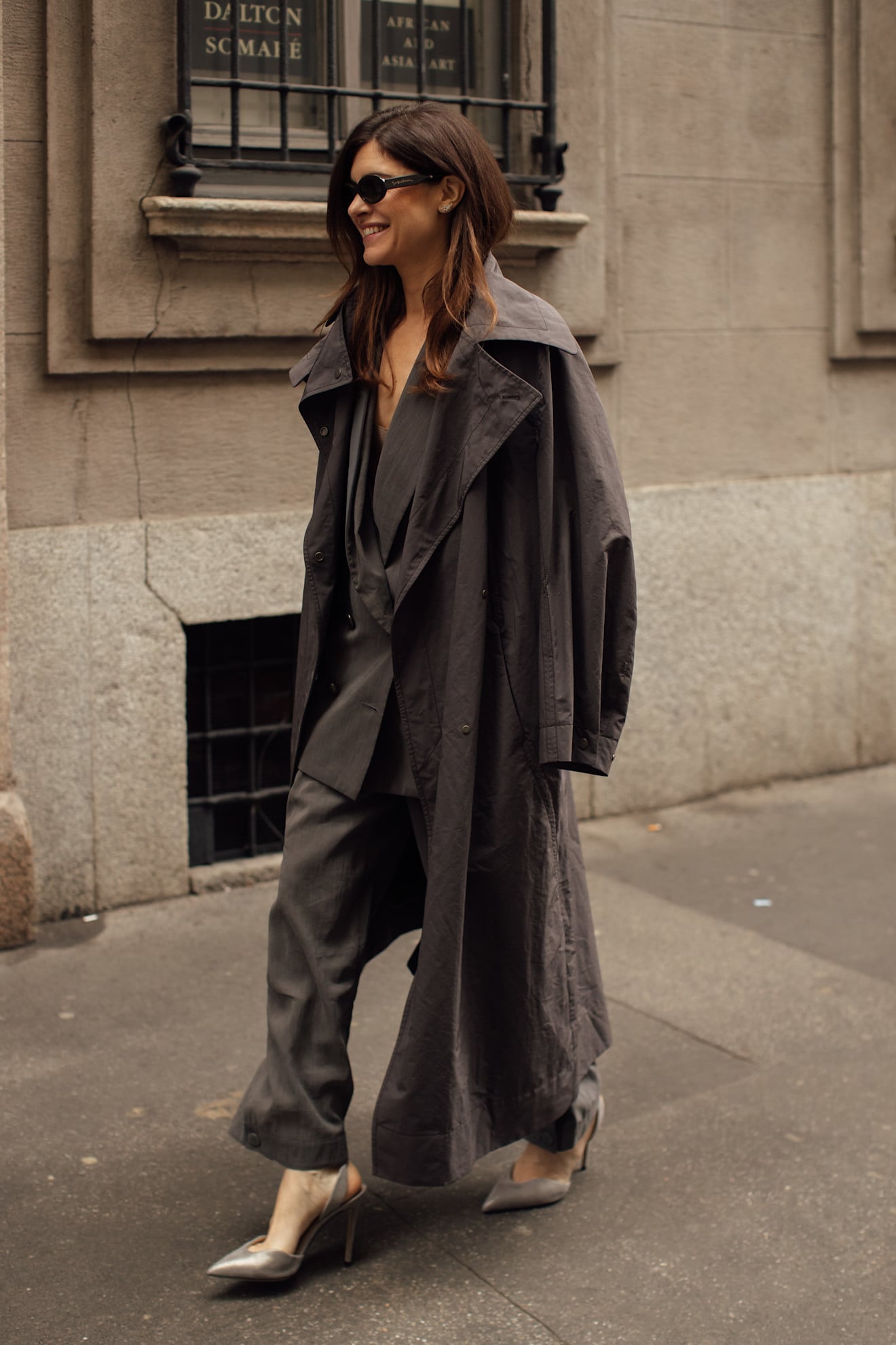 A woman wearing a loose fitting grey nylon trench coat with a belt
