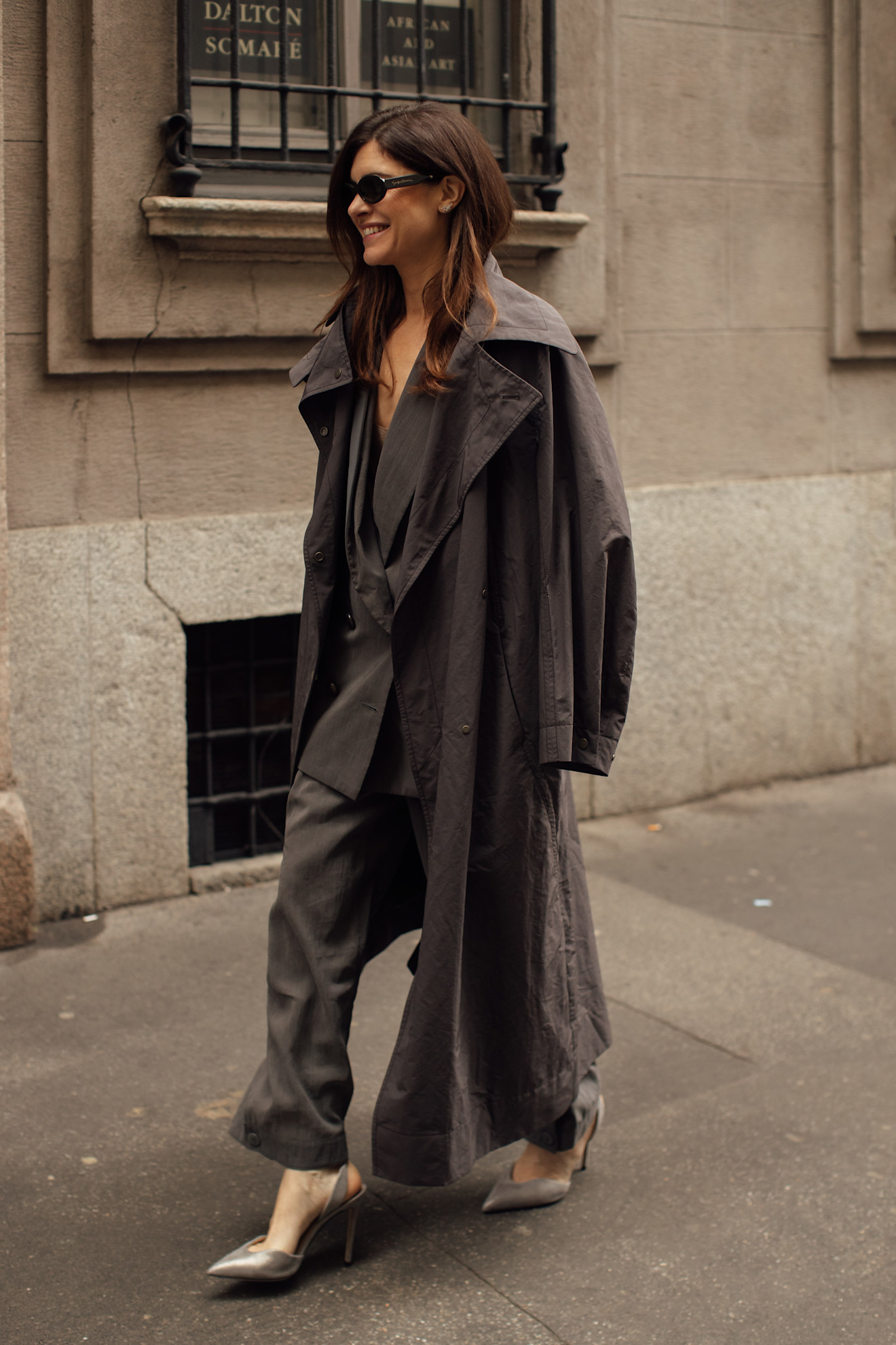 A woman wearing a loose fitting grey nylon trench coat with a belt